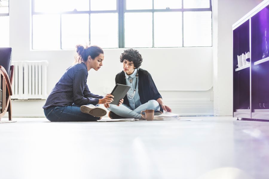 Two people sitting on a floor looking at a tablet together