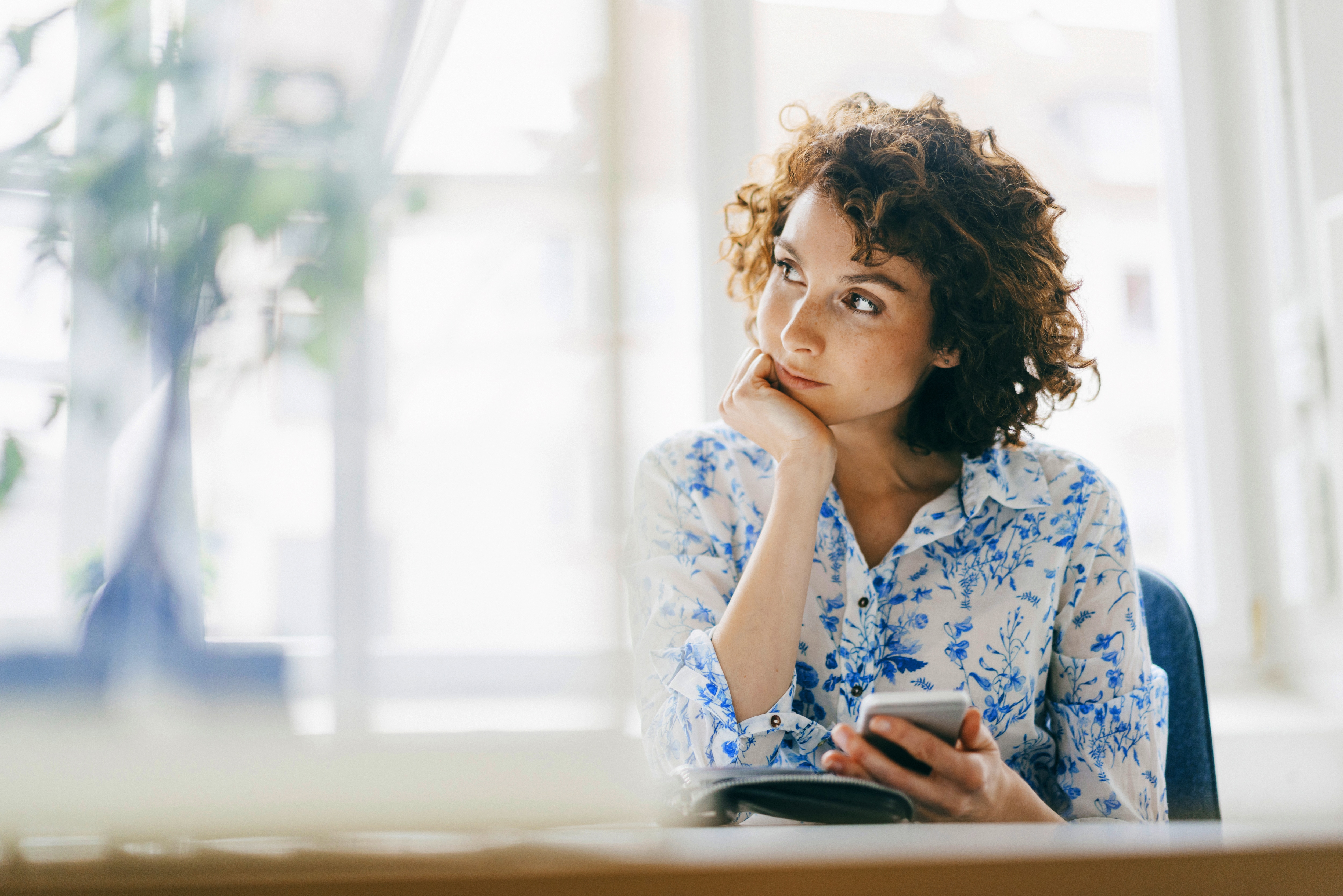 Woman looking to the side with her phone in her hand resting her chin on her hand