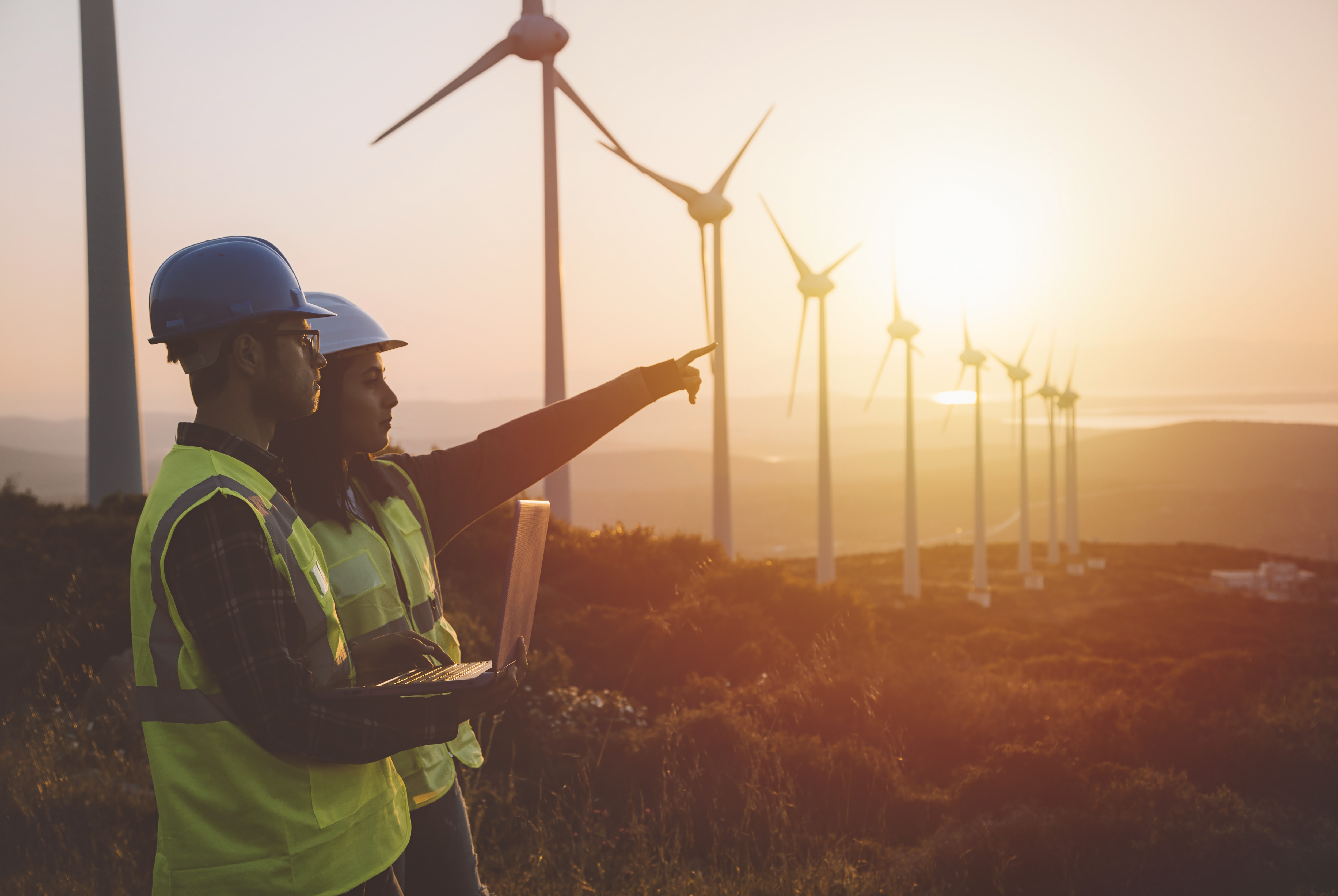 Workers outside at a windmill farm during sunset