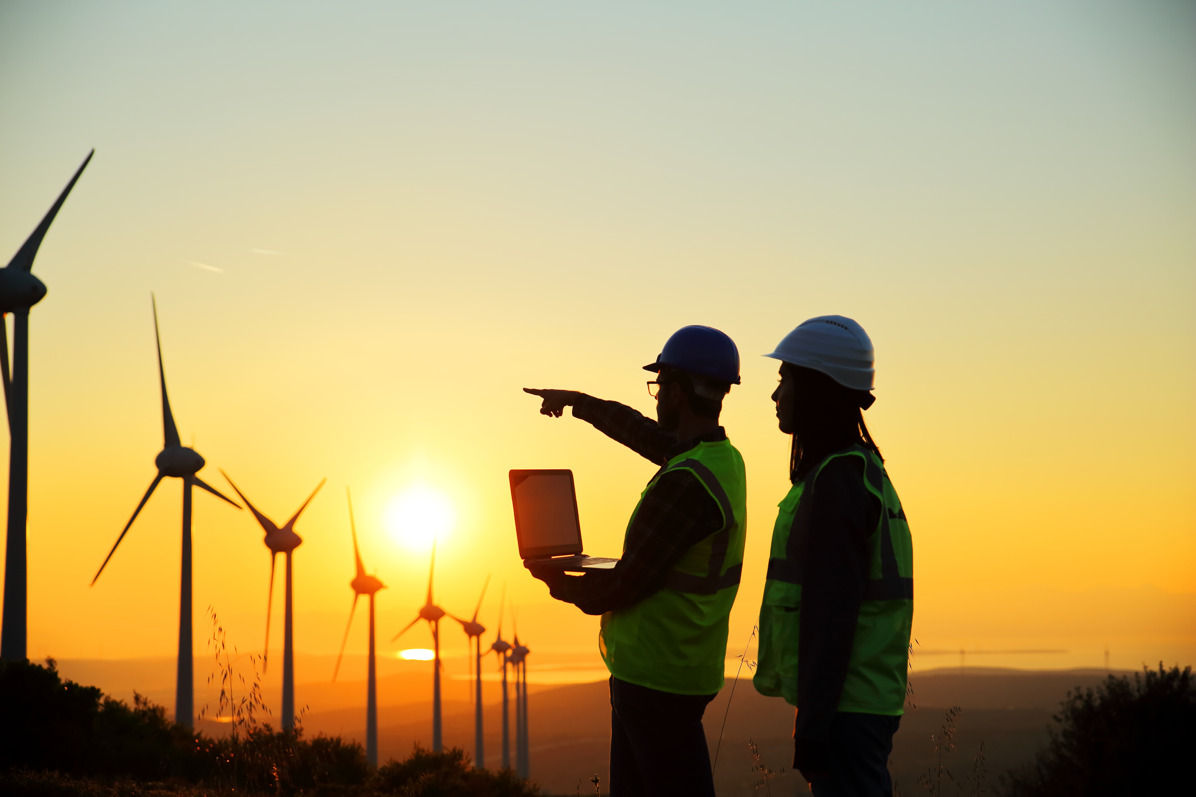 Two utilities workers pointing at windmills in the distance