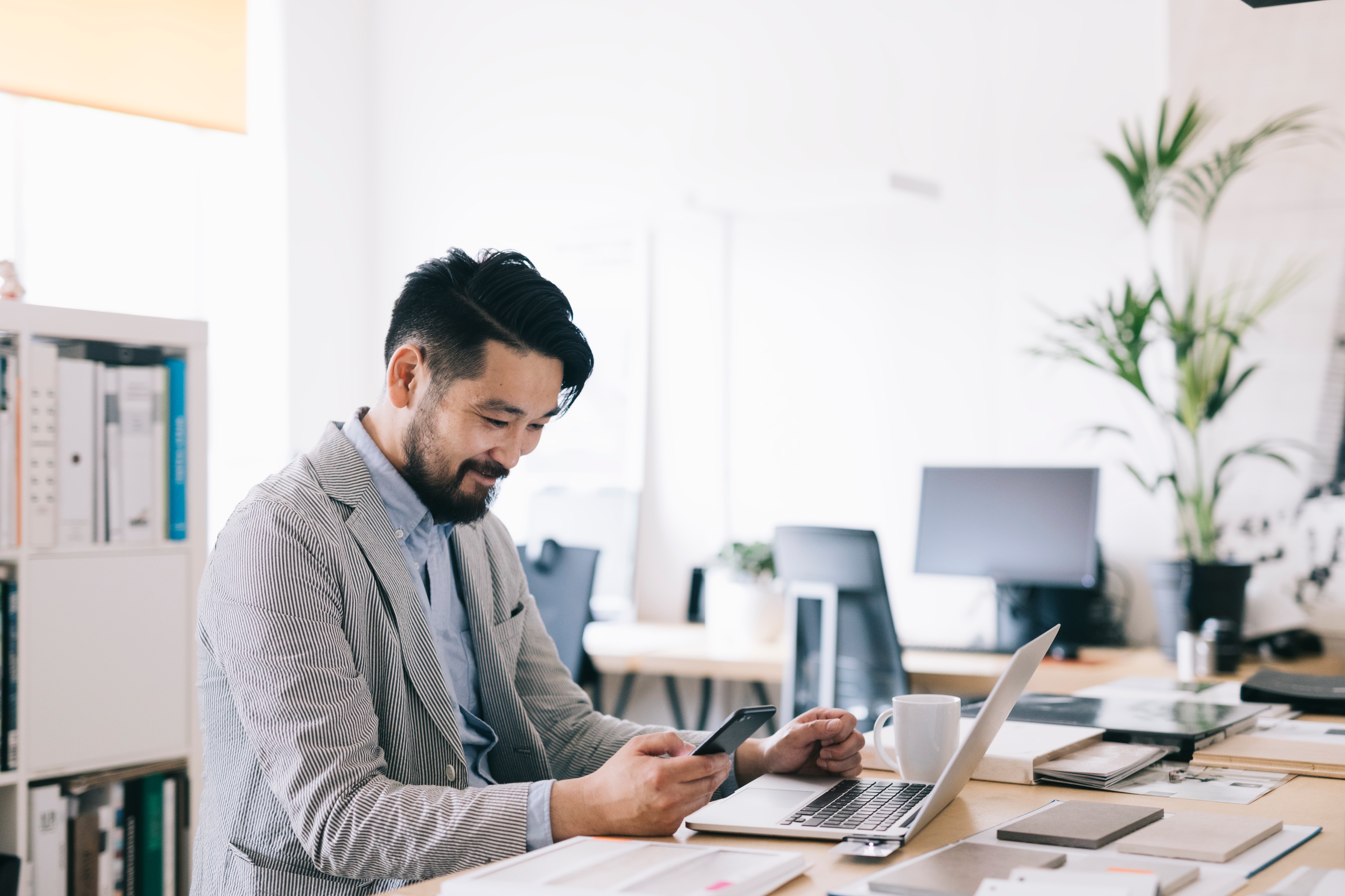 Man in office with laptop open and looking at phone