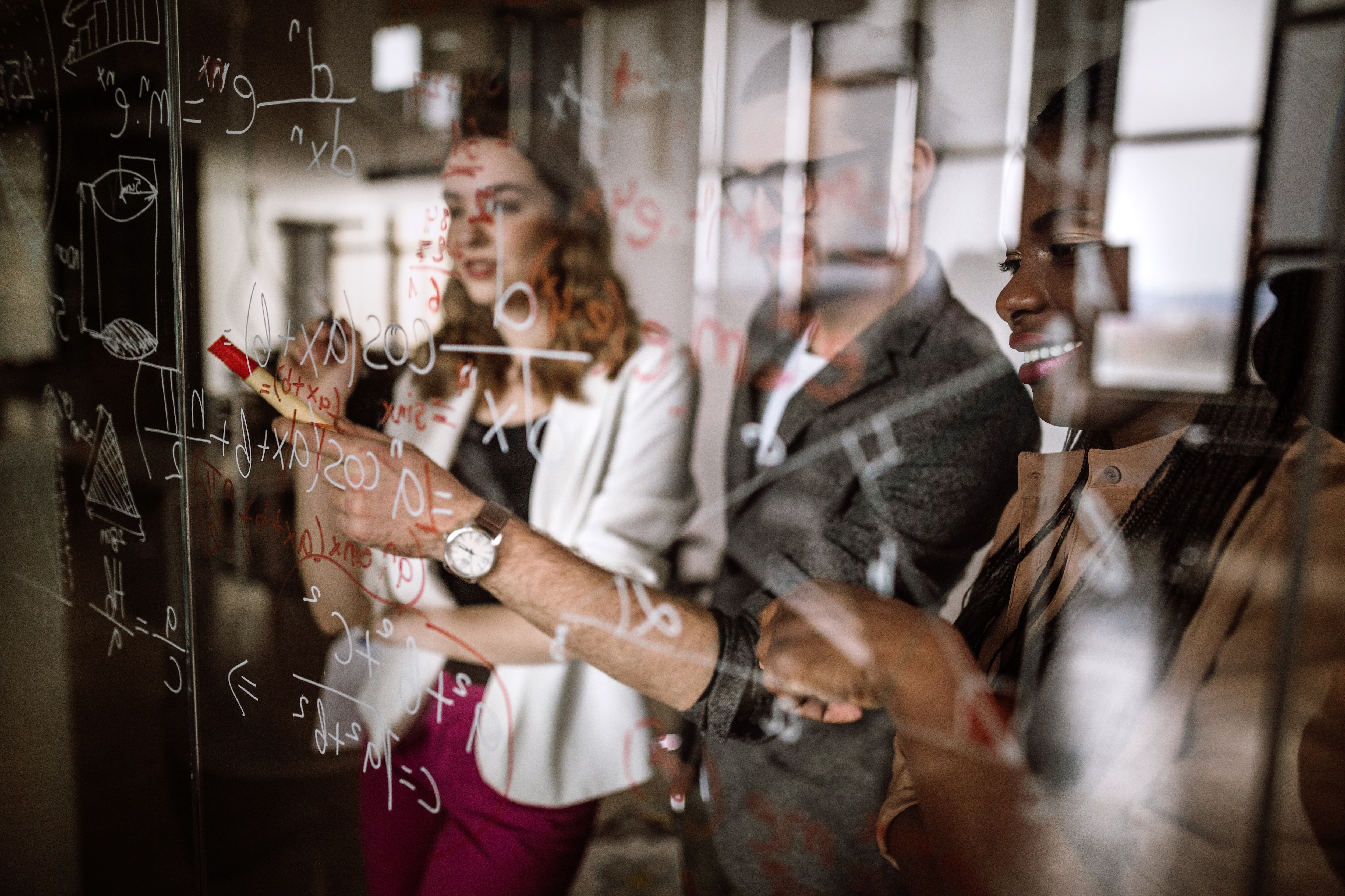 Two people solving a math equation on a clear, window like whiteboard