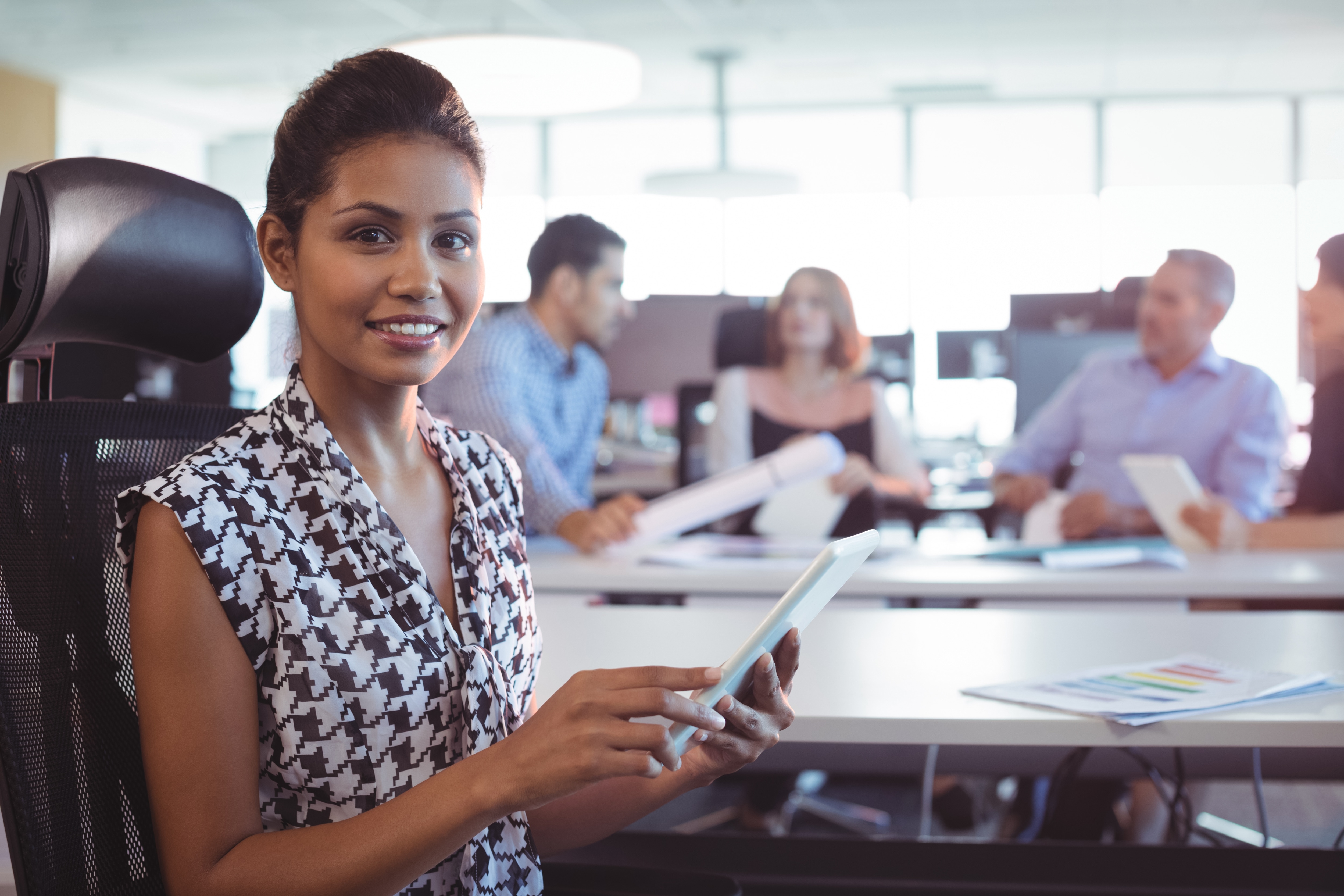 Woman sitting at desk with a clipboard and coworkers in the background