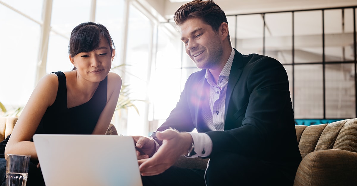 A man and woman look at a laptop screen while seated in an office