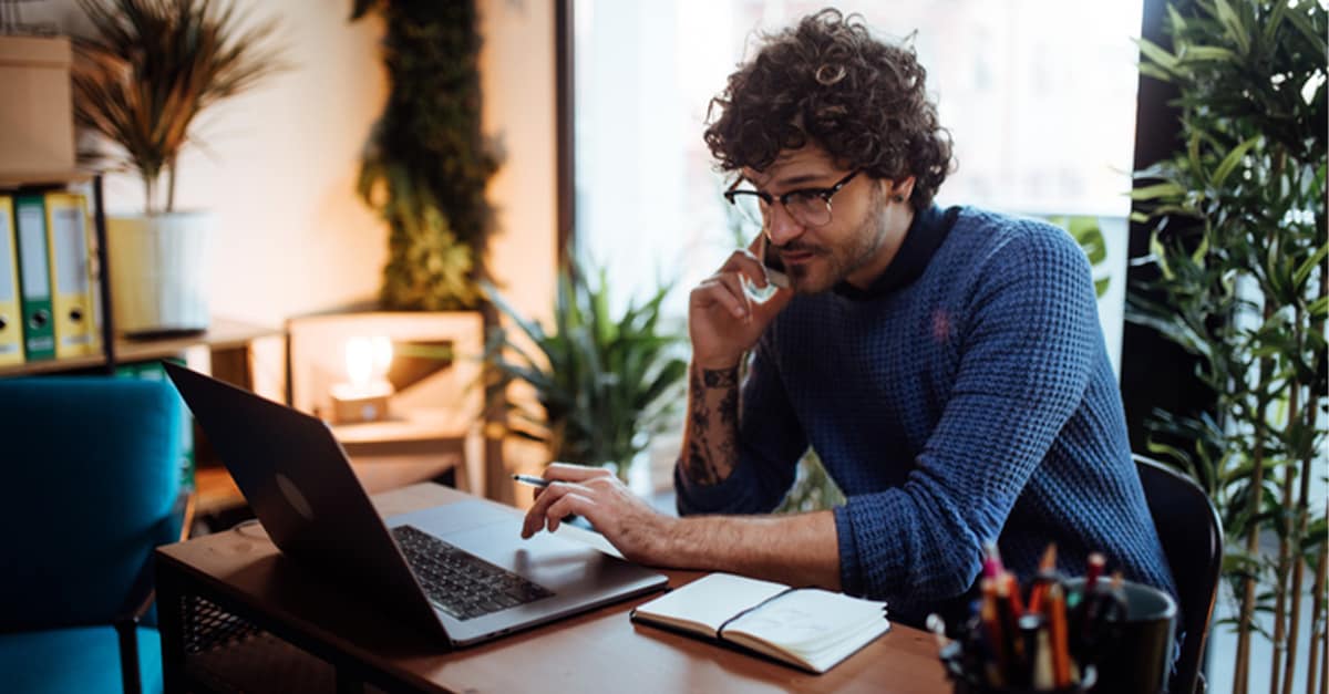 Man sitting at a desk looking at computer and talking on the phone