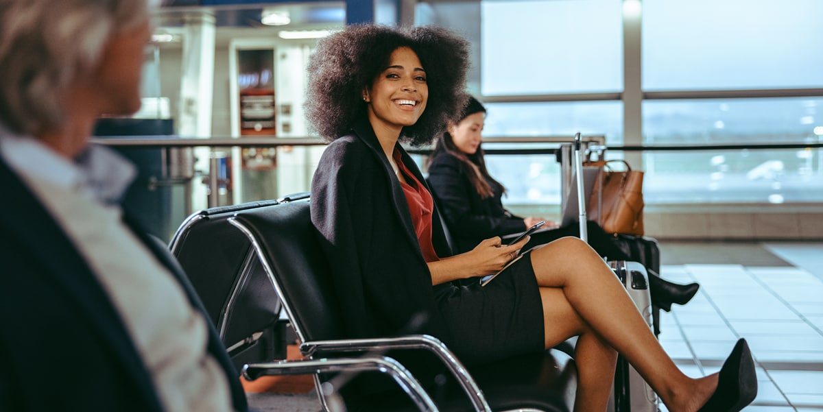 Smiling woman sitting at an airport holding her phone. 